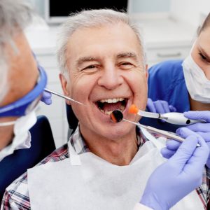 Our Grosse Pointe dentist can be an ally in the fight against oral cancer. In this image, dental professionals inspect a smiling man's teeth.