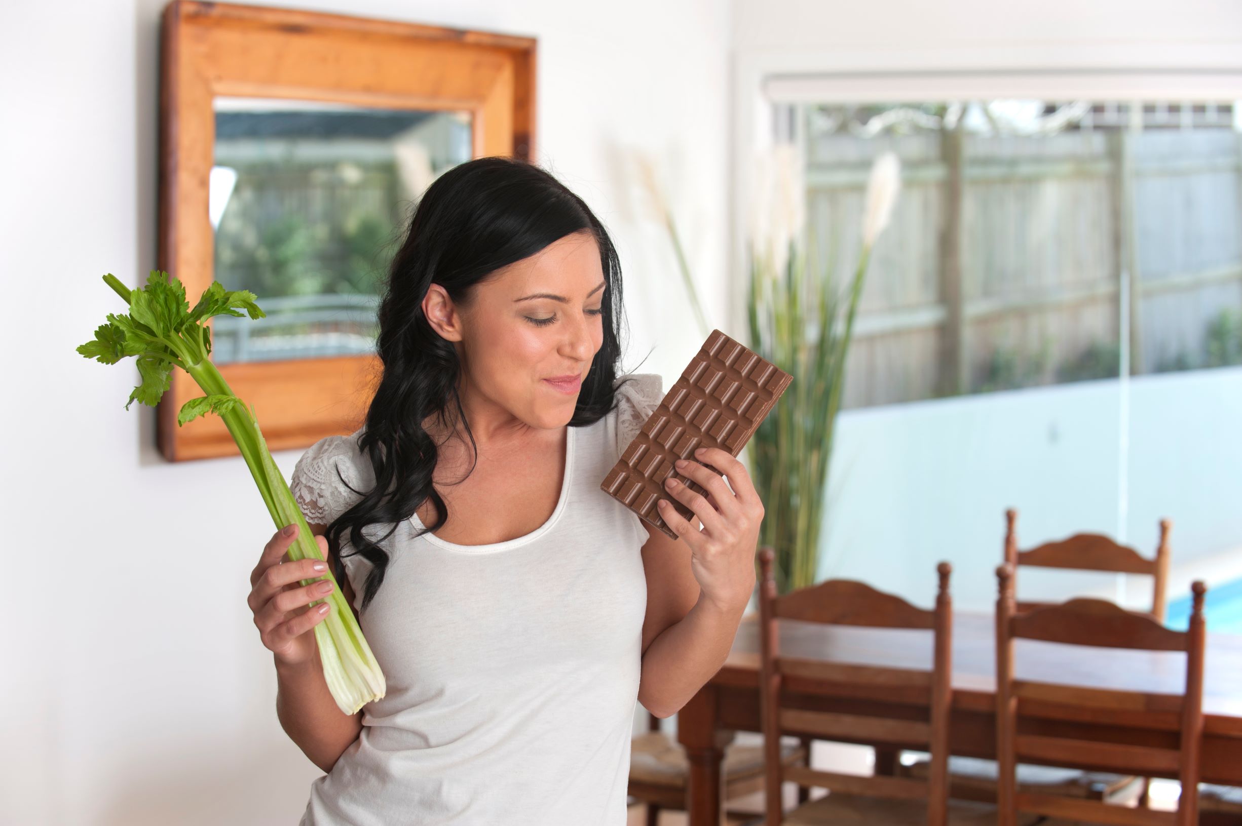 While the woman in this picture is debating between a block of chocolate and a large stick of celery as a snack, you can have both. While chocolate is a sugary and acidic food that can damage your teeth, celery is among the foods that can neutralize acids in your mouth.