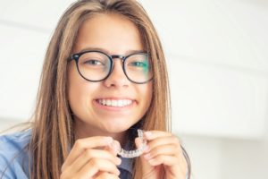 You’re beautiful no matter what, but straightening your teeth may make you feel even better. In this image, a young girl holds a tooth straightening mold while smiling.