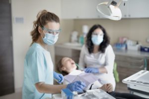 Will a tooth abscess cause a sinus infection? It's possible, and the tooth infection may even lead to heart disease. In this image, two dental professionals are assisting a patient in a dental chair.