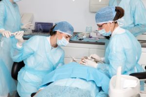 Studies show dentists' heightened COVID-19 prevention safety measures work. We take many precautions in our Grosse Pointe dental office. This image shows dental professionals in additional personal protective equipment working on a patient's dental concern..