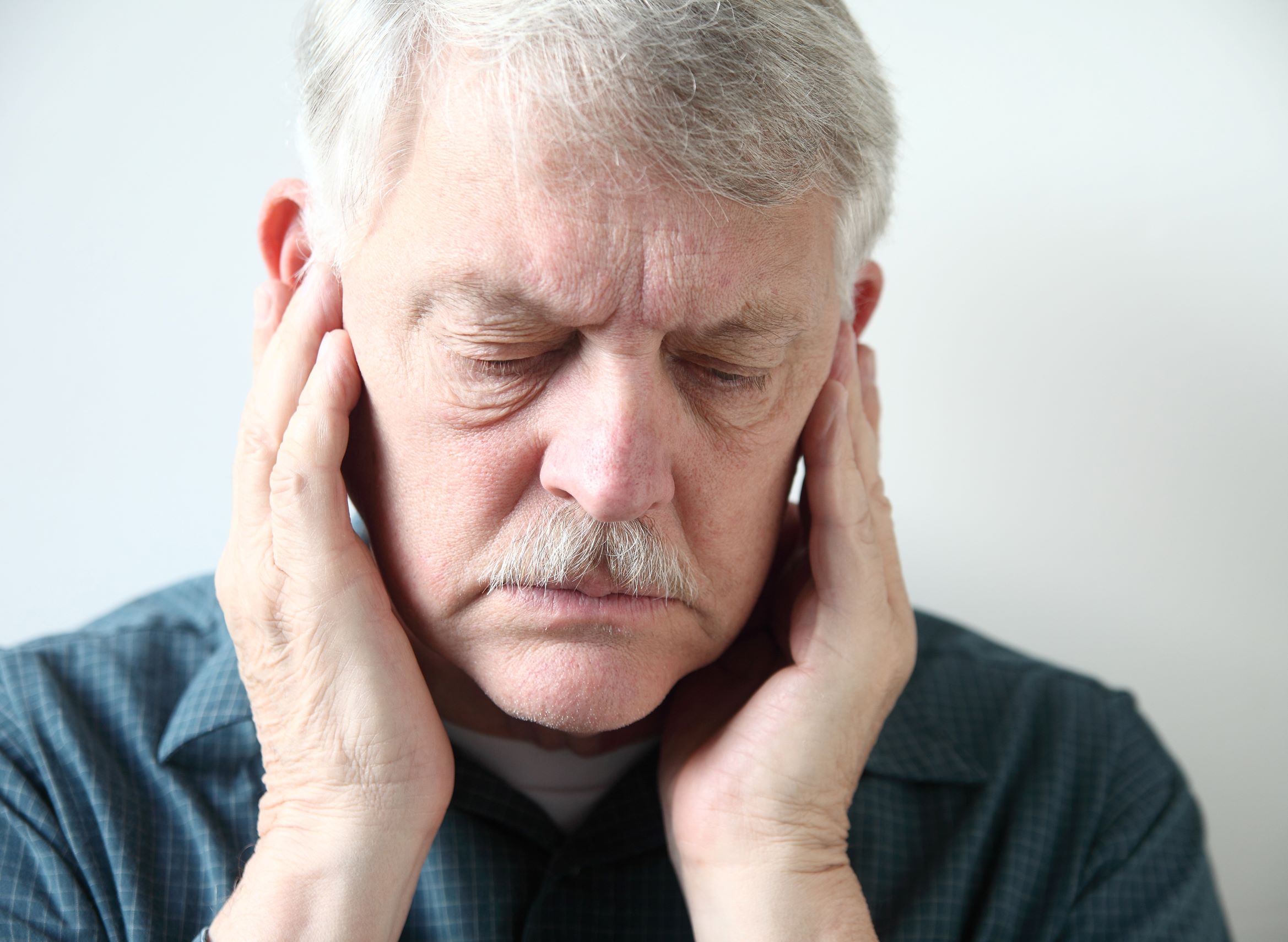 TMJ exercises can help treat jaw pain. In this image, a man is shown with his hands on his cheekbones to indicate jaw pain or a headache due to TMJ.