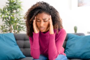 Temporomandibular joint dysfunction can lead to headaches, as depicted in this image of a woman sitting on a couch with a headache.