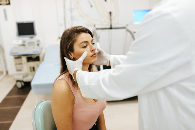 Your sinuses and your oral health affect one another in numerous ways. In this image, a doctor places his hands on a woman's face to diagnose her condition.