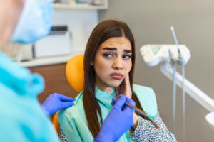 A woman holds her jaw in pain at the dentist's office. There are many signs of a tooth fracture vs. a cavity.