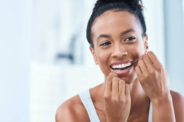 African American woman flossing teeth in the mirror